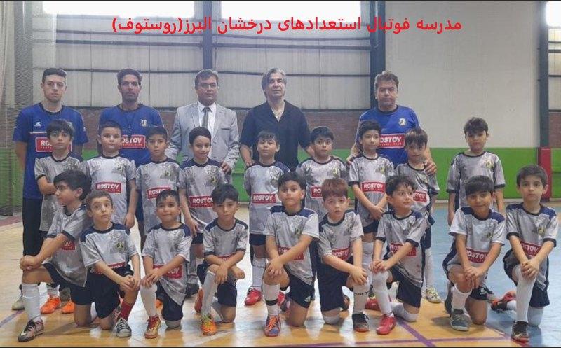 عکس تیمی فوتبالیستهای نونهال مدرسه فوتبال روستوف کرج با لباسهای طوسی در سالن ورزشی به همراه مربیان و مدیر و فوتسالیست ملی پوش