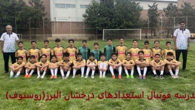 عکس تیمی فوتبالیستهای نوجوان مدرسه فوتبال استعدادهای درخشان البرز با لباسهای طلایی در زمین چمن در کنار دو مربی خود با لباس سفید