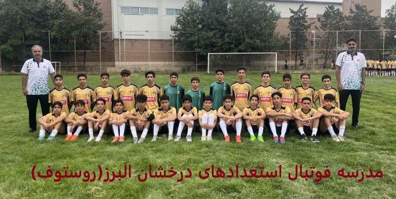 عکس تیمی فوتبالیستهای نوجوان مدرسه فوتبال استعدادهای درخشان البرز با لباسهای طلایی در زمین چمن در کنار دو مربی خود با لباس سفید